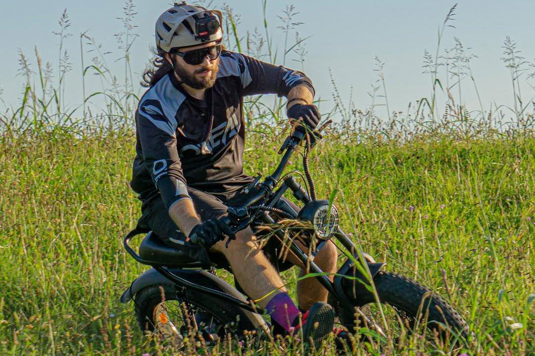 Man riding Z8 Electric Bike in grassy field with helmet and sunglasses.