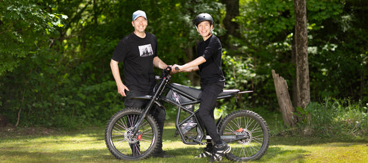 Father and son enjoying Father's Day Challenge ride together on a black ebike in a forest setting