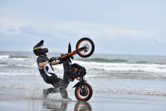 Riding Times GT54 eBike performing a wheelie on the beach with water splashing around
