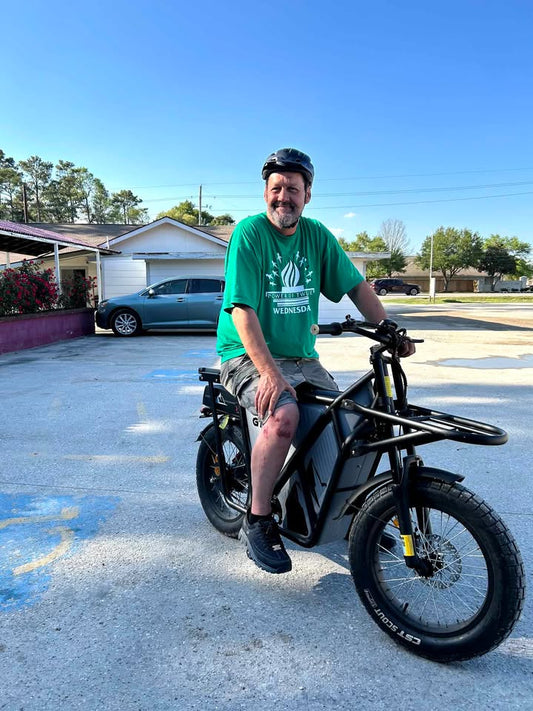 Man wearing a helmet sitting on a black RIDING TIMES GT53 cargo e-bike with visible knee injury outdoors under clear sky, demonstrating e-bike safety.