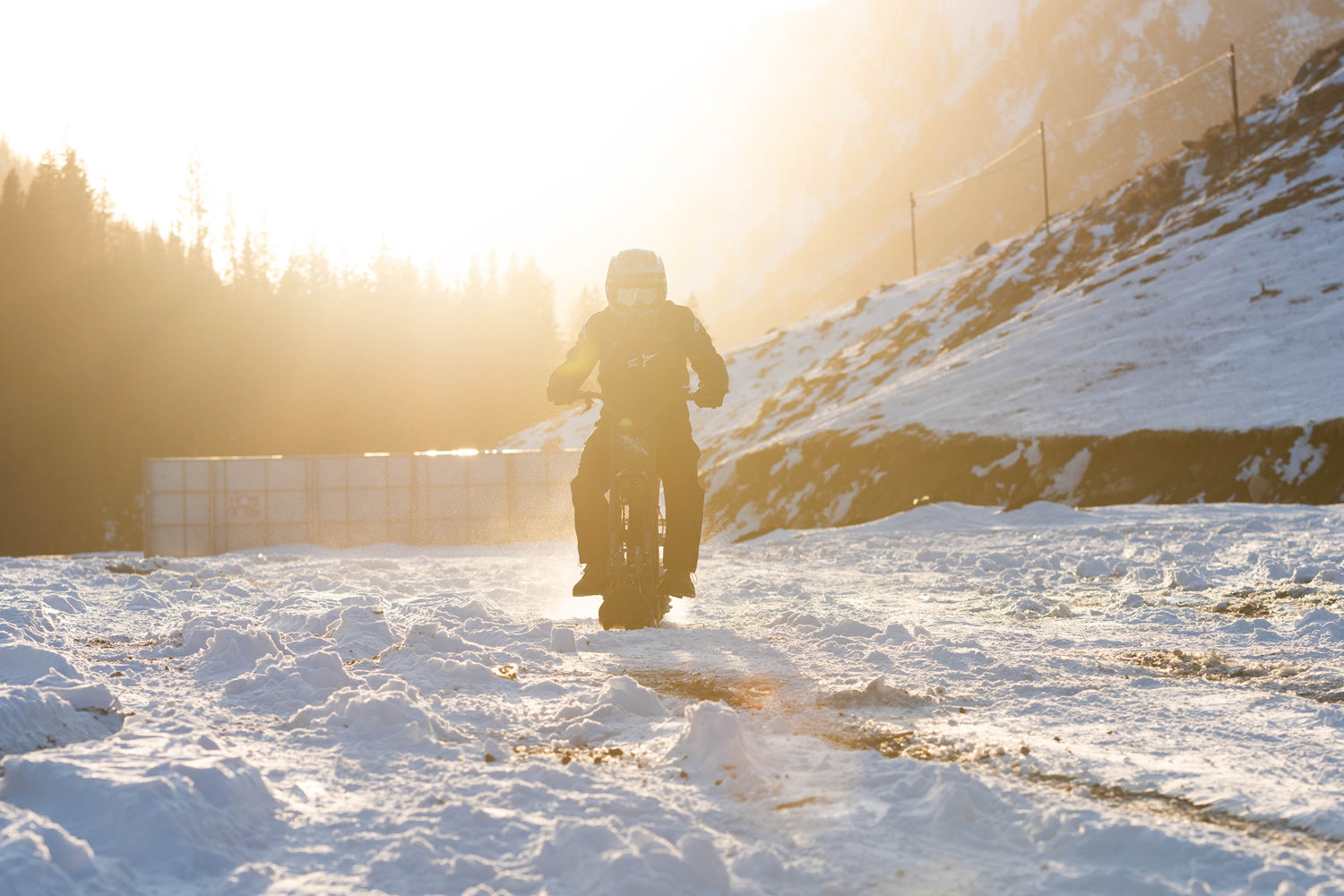 Person riding a motorcycle on a snowy landscape with a sunset in the background